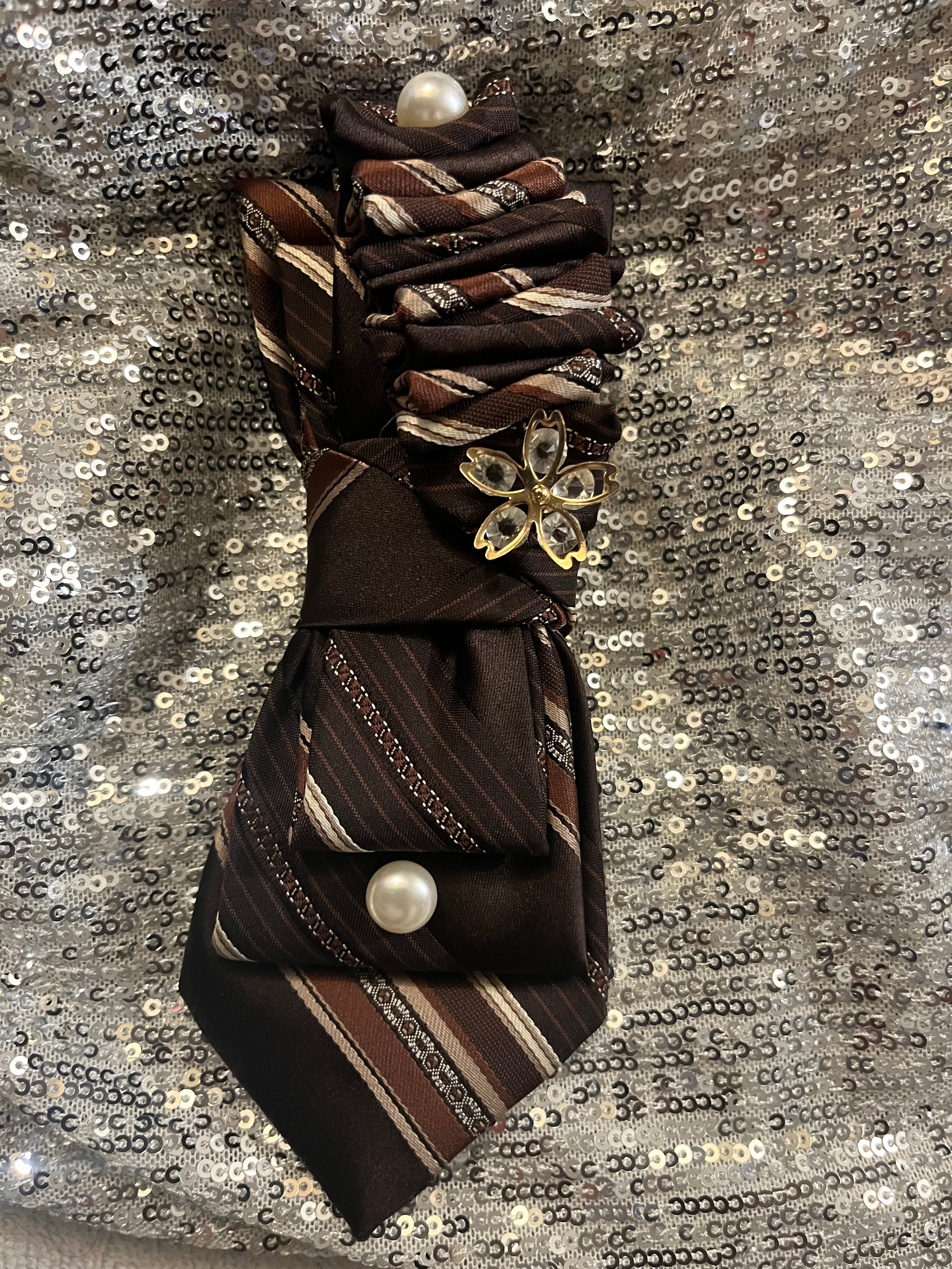 Brown striped tie with gold crystal butterfly charm and pearl accents on silver sequin background